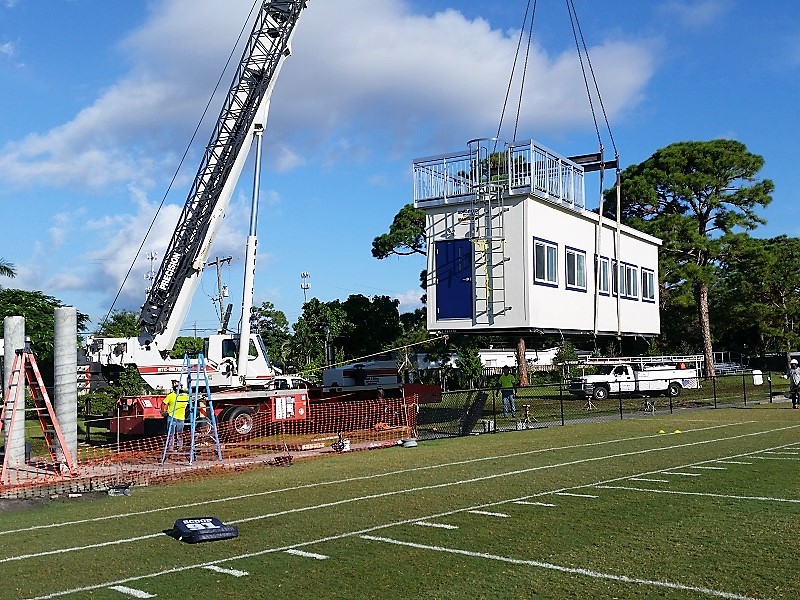 Picture of modular press box being lifted onto piling foundation with crane